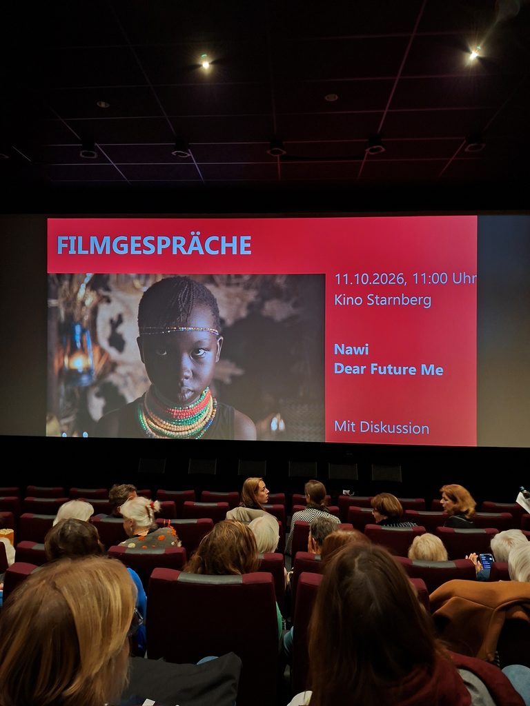 Das Publikum sitzt in einem dunklen Kinosaal vor einer großen Leinwand, auf der eine Ankündigung zur Filmvorführung von Nawi: Dear Future Me am 11. Oktober 2026 im Kino Starnberg zu sehen ist.